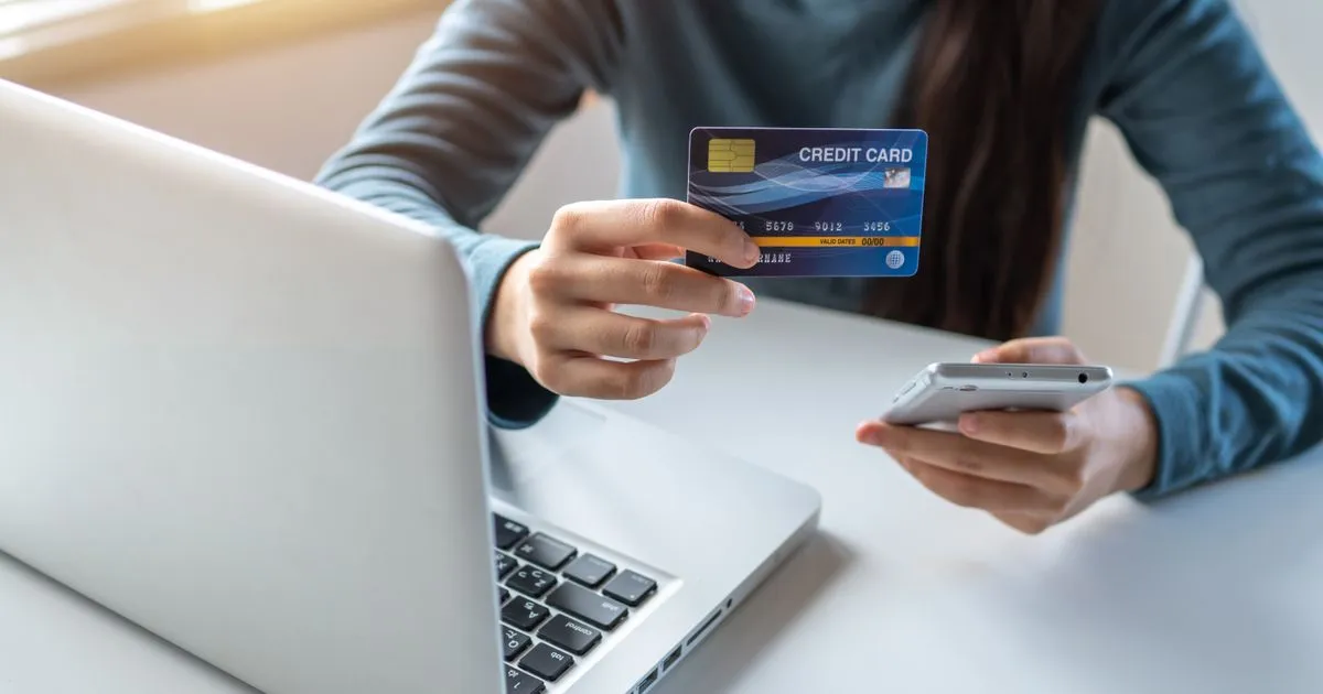 クレジットカードとスマートフォンを手に、ノートパソコンで買い物をしている様子