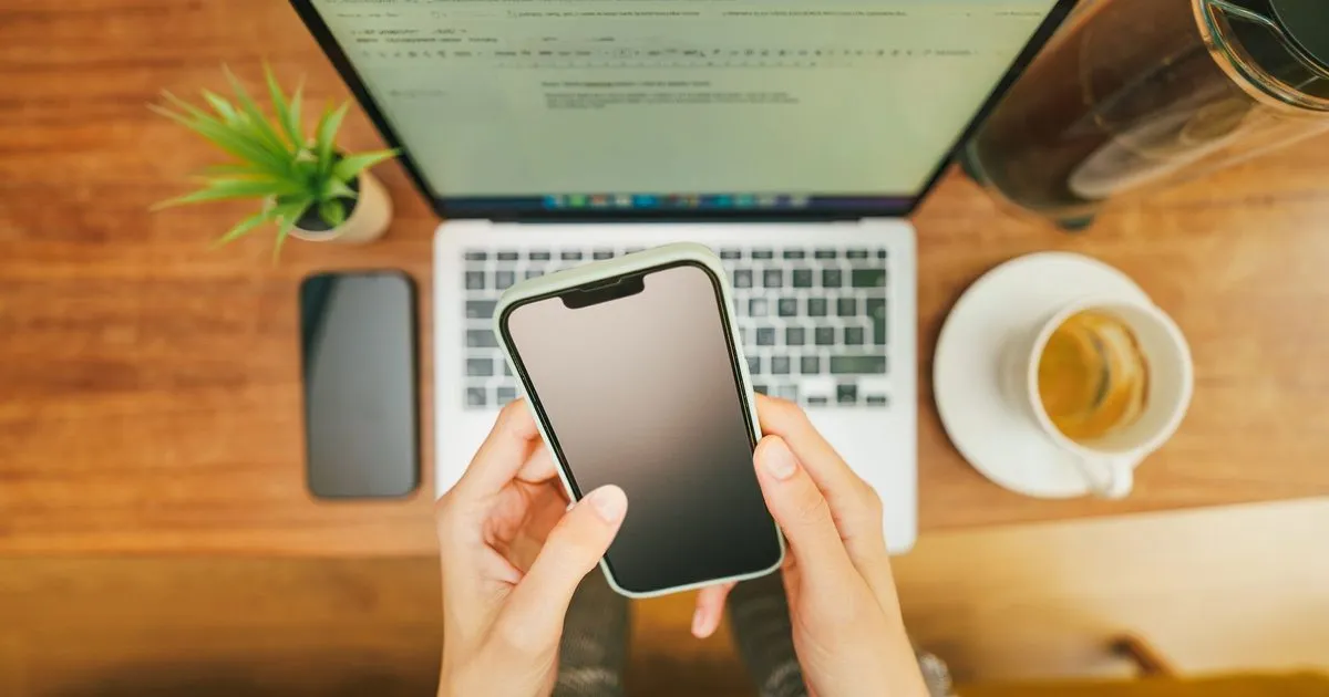 ノートパソコンの前でスマートフォンを操作している手元