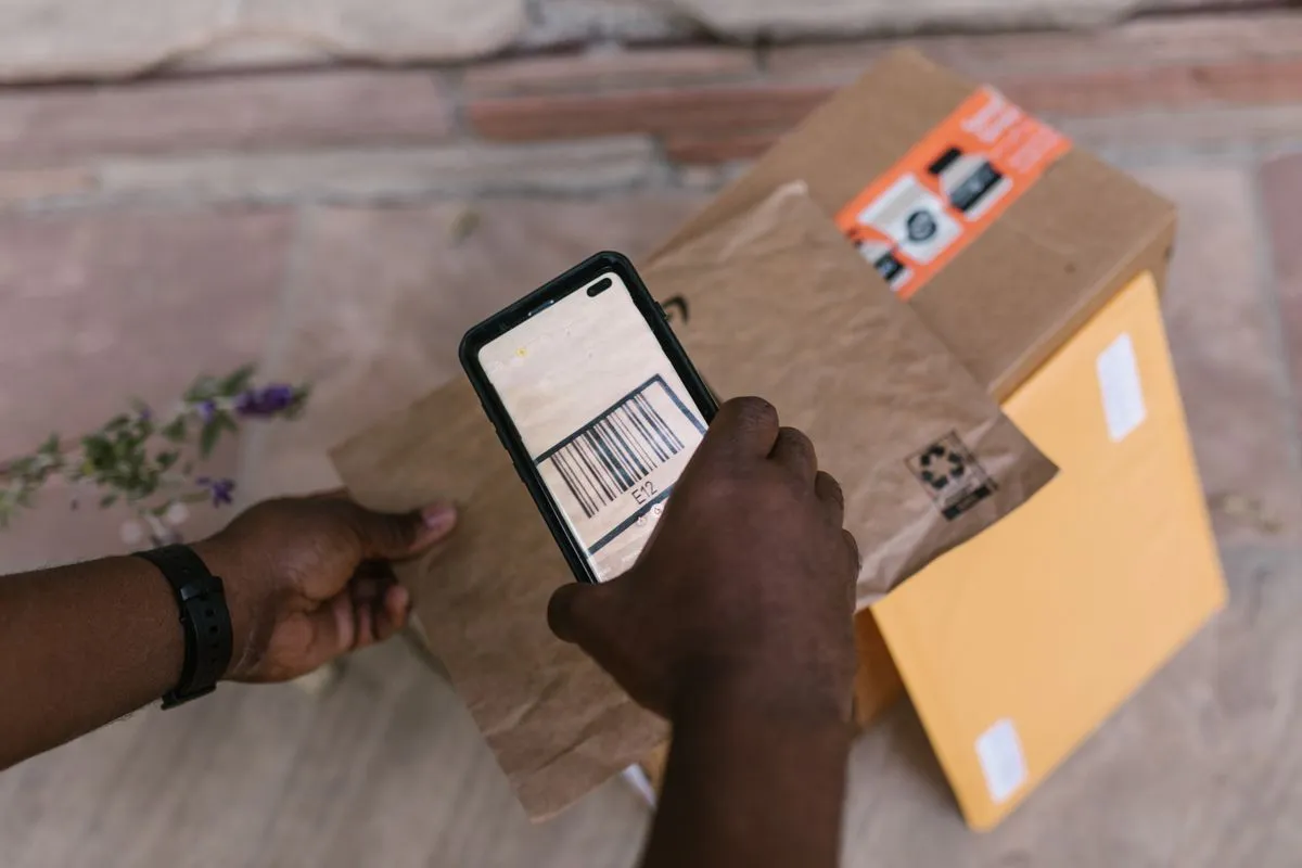 スマートフォンのカメラで段ボール箱に貼られた荷物のバーコードを読み取っている手元