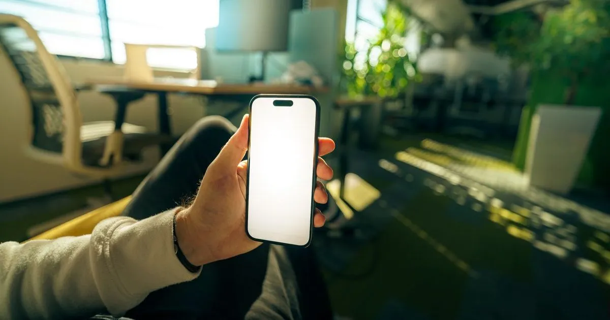 白く光る画面のスマートフォンを片手で持っている手元